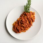 Immagine di un piatto di ragù con vino rosso sullo sfondo, evidenziando la preparazione culinaria.